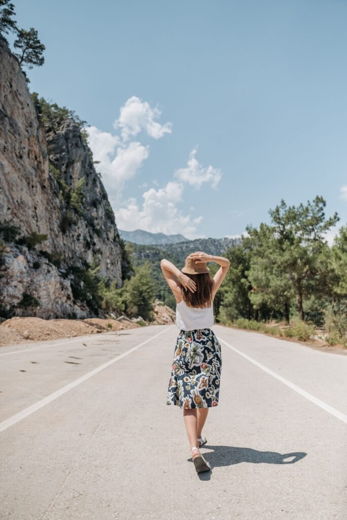 A woman in a stylish outfit walks along a mountain road during summer.